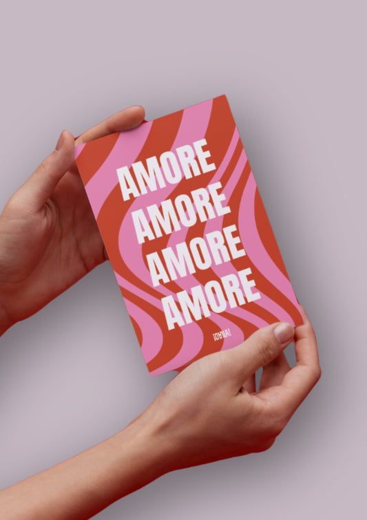 Photo produit d'une carte prise dans les mains d'une femme sur fond neutre. La carte a pour design un fond rose et rouge en vague, avec l'inscription Amore au centre décliné en 4 fois. En bas se trouve le logo de la marque OLALA.