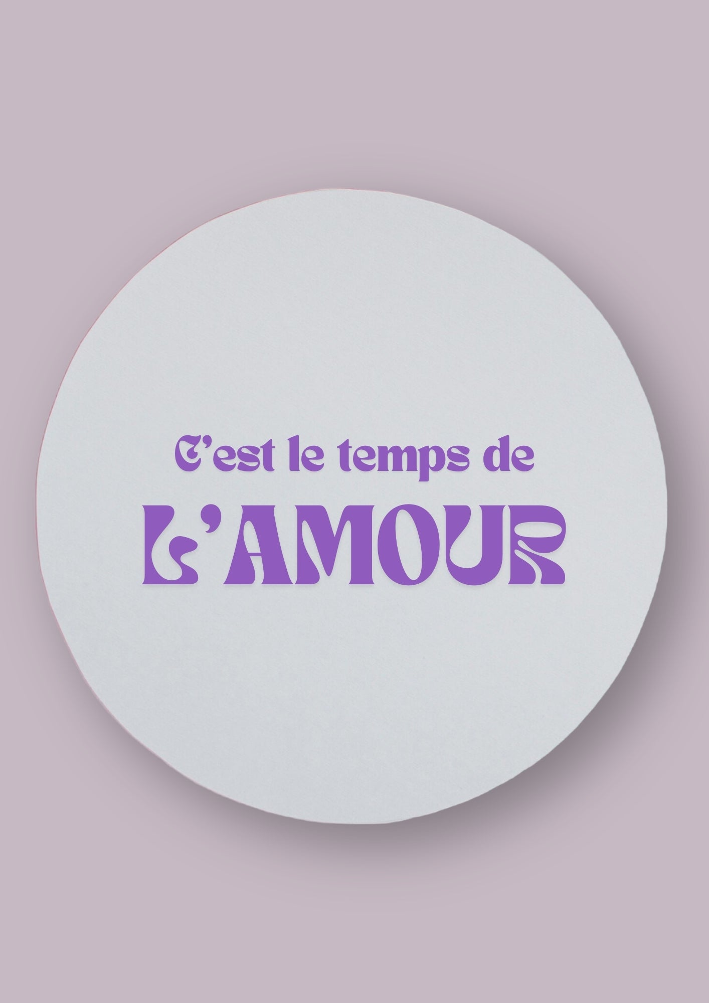 Miroir rond avec la phrase c'est le temps de l'amour écrite en violet. Le fond de la photo est de couleur neutre.