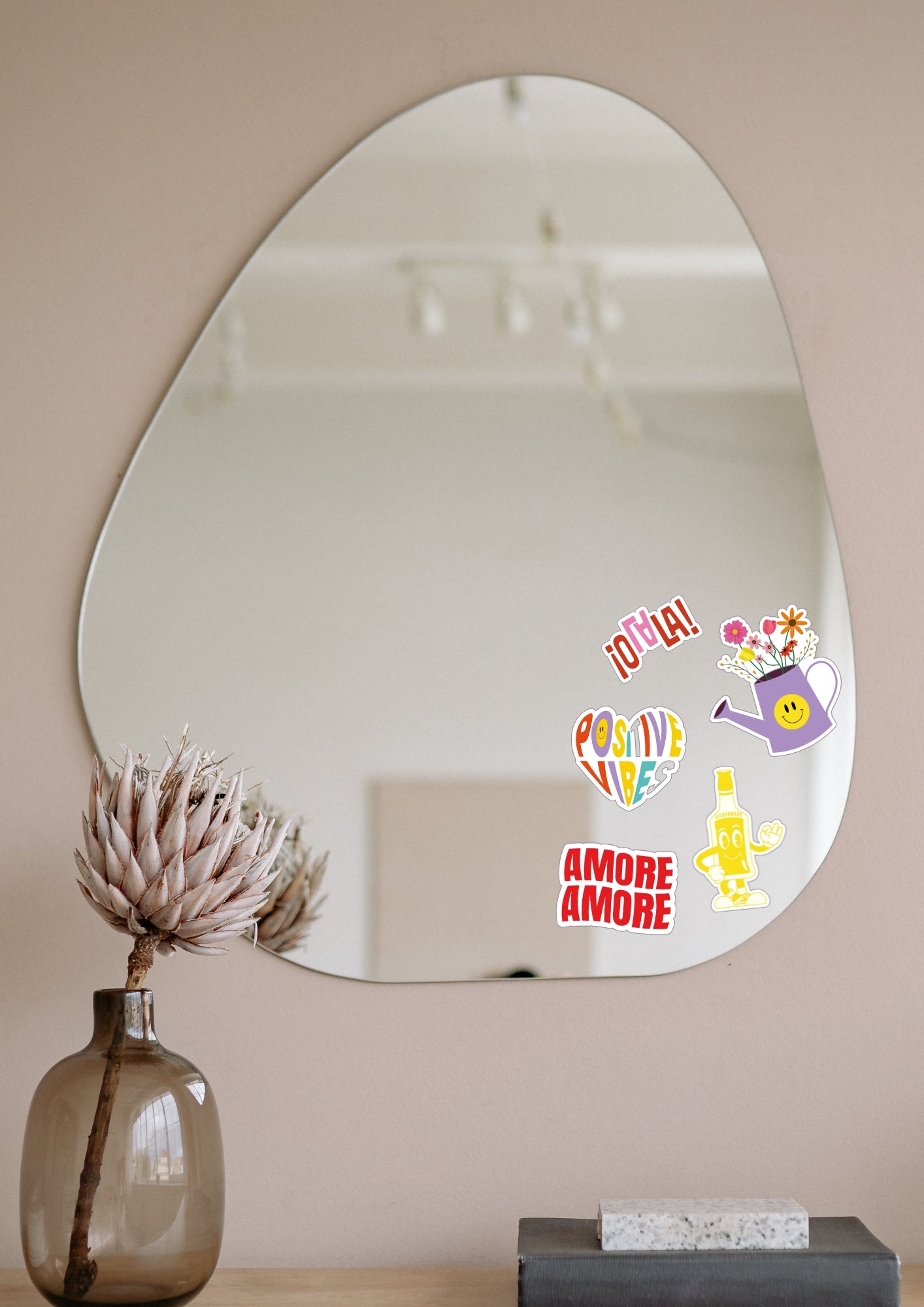 Miroir en forme de goutte d'eau accroché à un mur blanc sur lequel cinq stickers sont collés dessus.