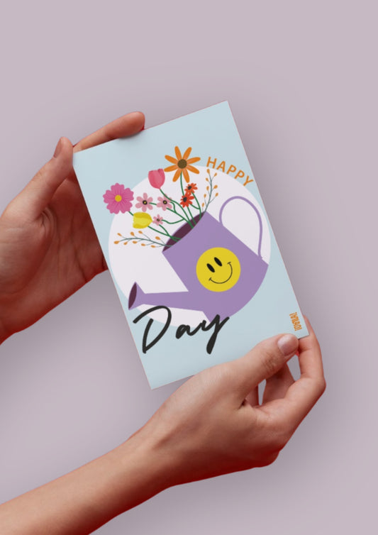 Carte avec fond bleu, un cercle blanc au centre, un arrosoir violet avec un smiley jaune dessus. Un bouquet de fleur sort de l'arrosoir. 