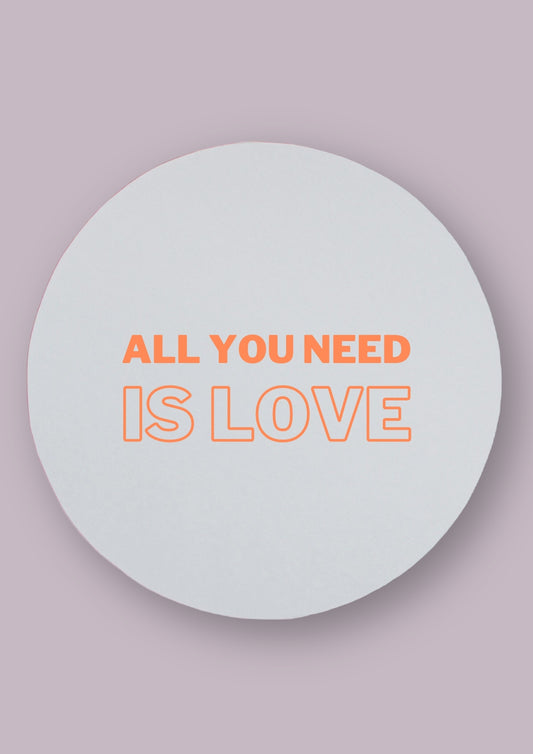 Miroir rond avec la phrase All you need is love écrite en orange dessus. Le fond est neutre.