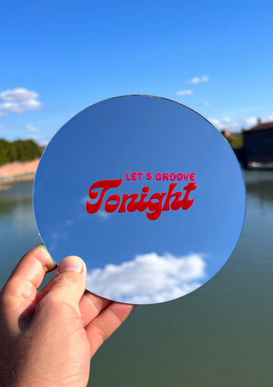 Miroir rond tenu dans une main avec une phrase en son centre où il y a écrit let's groove tonight. En fond le ciel bleu et la garonne à Toulouse. 