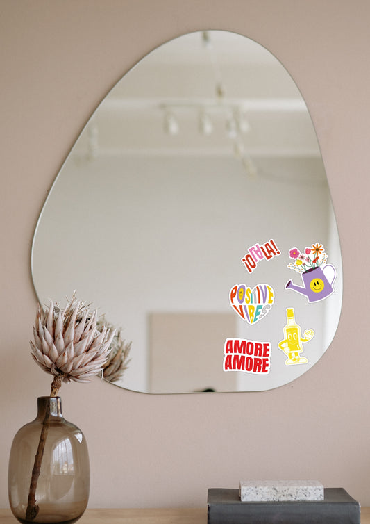 Miroir en forme de goutte d'eau accroché à un mur blanc sur lequel cinq stickers sont collés dessus.