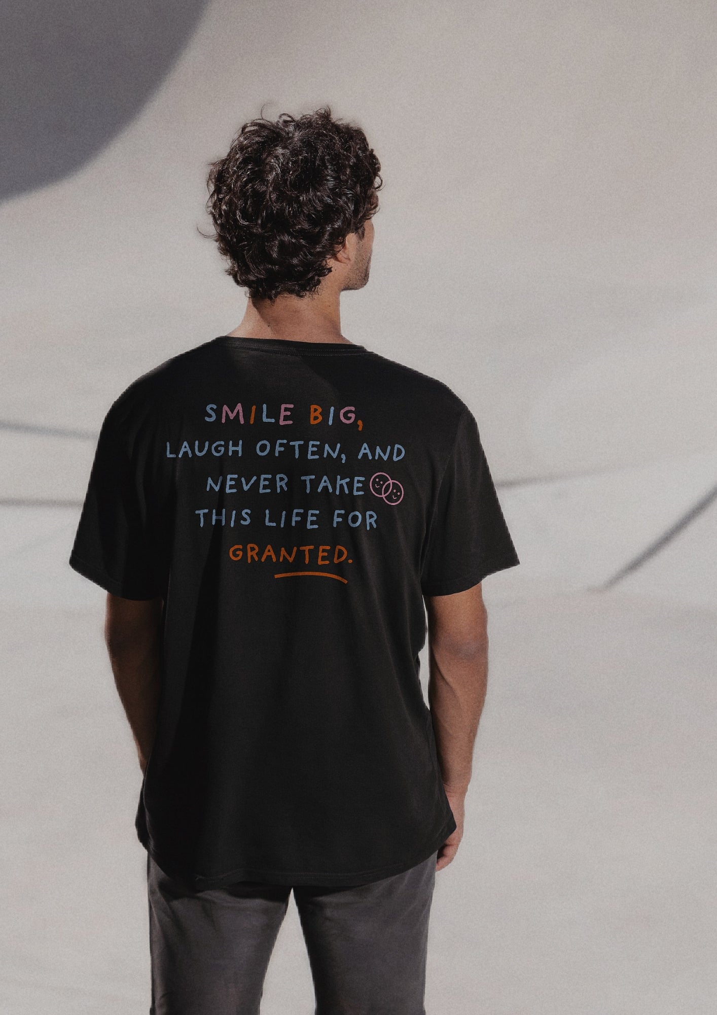 Mannequin homme de dos qui porte un t-shirt noir avec la phrase "smile big, laugh often, and never take this life for granted" écrite de plusieurs couleurs. 